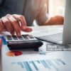 Persona che utilizza una calcolatrice accanto a documenti finanziari per valutare i costi di un prestito
